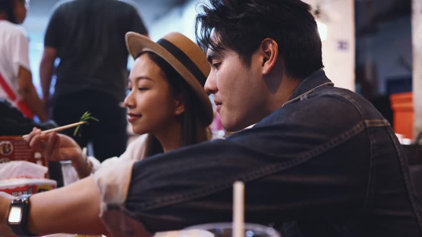 Young Asian couple traveler tourists eating Thai street food together in China town night market in Bangkok, Thailand