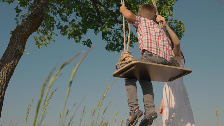 Family holiday, Mom shakes her son on swing, child in park. Mother son play, happy child swings on swing in summer. Weekend with family. Child, boy is flying on swing. Childrens entertainment in park Royalty-Free Stock Footage #1105425553