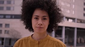 Young beautiful African American girl serious looking at camera and afro hair. Confident and earnest millennial woman posing for video. Latin people with negative expression outdoors.