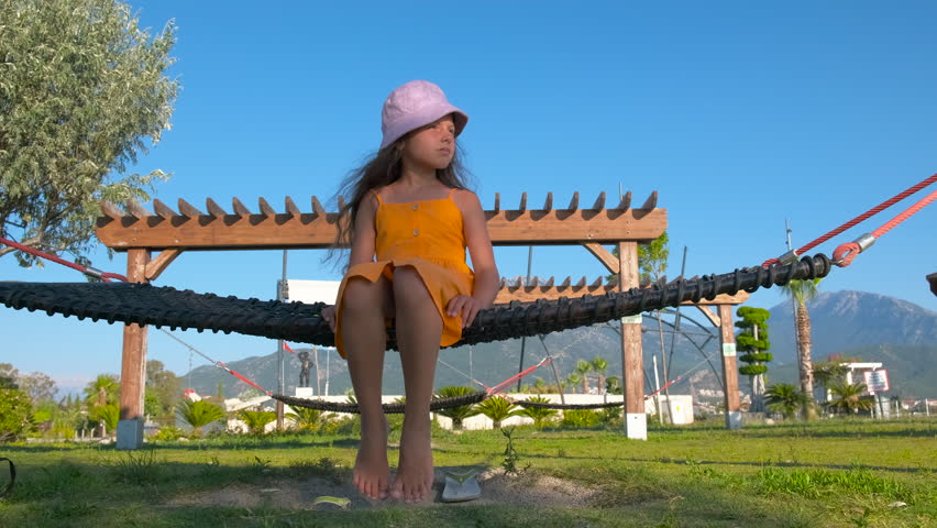 Happy child on hammock on meadow. A view of little child traveler sitting in hammock in the green summer park during holidays.