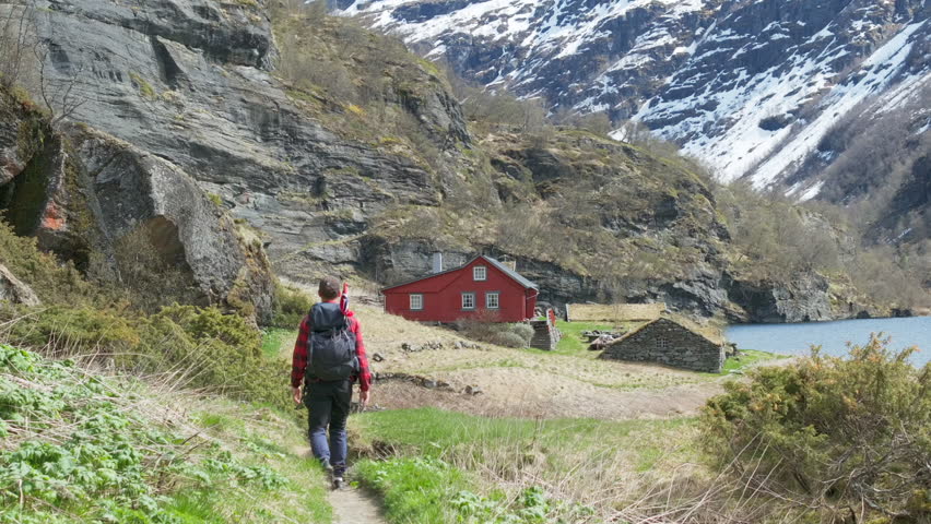 Male hiker with Norwegian flag wander Aurlandsdalen canyon with lake cabin view