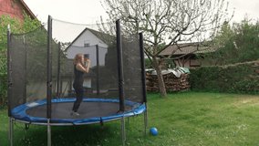 Girl is jumping on a trampoline in her backyard with green grass in the country house