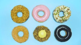 Top view different donuts colors changing at blue background. Stop motion creative video animation donut. Bakery concept glazed sweet desserts colorful donuts. Chocolate, pink, white donuts in 4K.