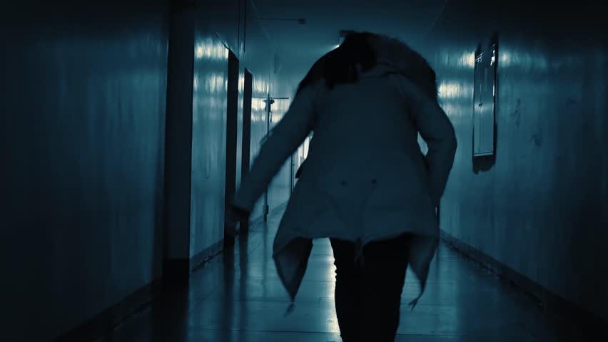 Frightened woman in a panic runs away from danger along a dark, scary corridor. Flickering sign with Russian text above the doors: exit. Royalty-Free Stock Footage #1105443527