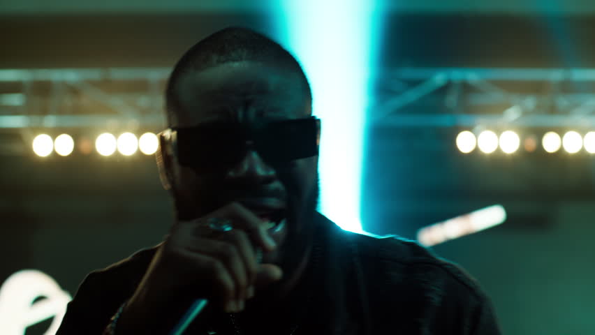 African-American Black rap artist performing his gig on a stage of a large venue, surrounded by bright flashig lights Royalty-Free Stock Footage #1105443851