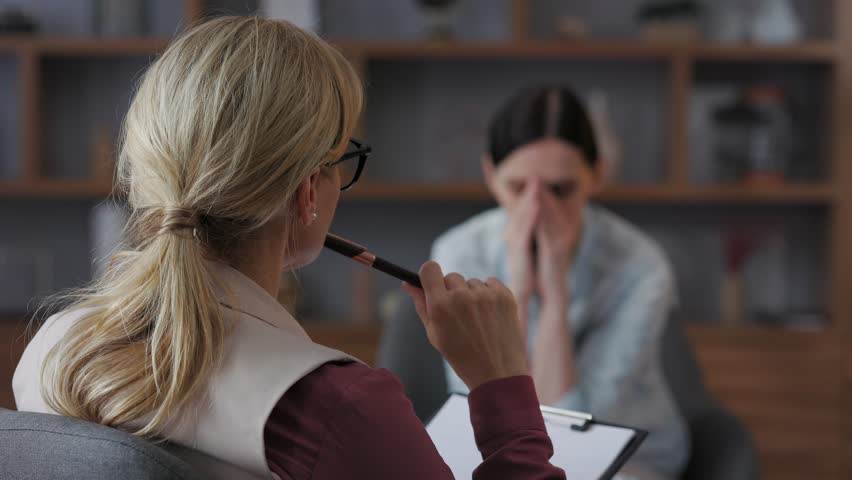 Over shoulder view of female psychologist sitting in armchair, talking with upset woman patient. Psychologist taking notes on clipboard. Psychology, mental therapy, mental health, therapy session. | Shutterstock HD Video #1105449643