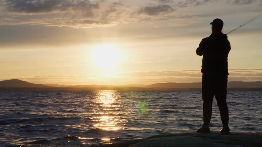 A fisherman catches fish at sunset with a spinning rod. Young guy on evening fishing on the lake. Royalty-Free Stock Footage #1105453075
