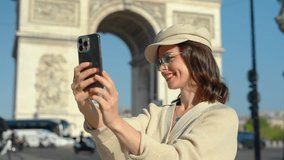 Smiling girl taking a selfie on a smartphone against the backdrop of the Arc de Triomphe