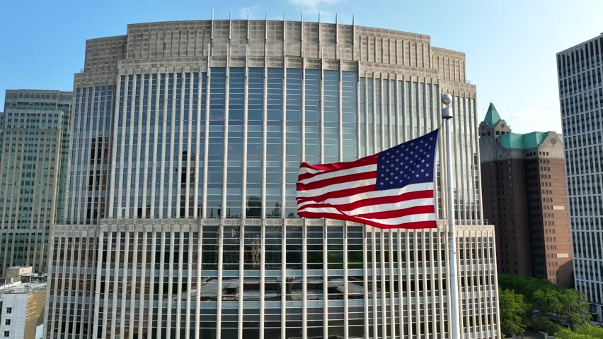 American flag waving in front of USA government building in large city in America. Aerial establishing shot of building in beautiful golden hour light. Offices for FBI, CIA, IRS, Social Security, etc. Royalty-Free Stock Footage #1105464009