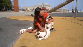 Two dogs and long haired teenager girl in playground park happy smiling. enjoying cuddling, petting two pets small white Jack Russell terriers friends, Summer in big city. Pets love and trust video