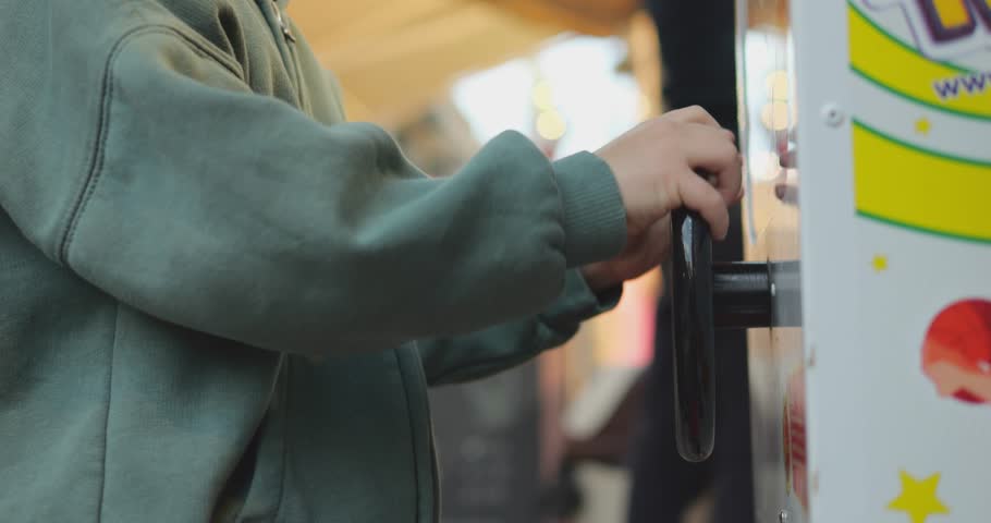 Close-up small boy hands turn steering wheel to play video arcade game machine. Unrecognizable elementary age child plays on coin operated kids street machine.