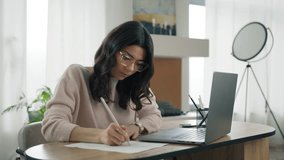 Young hispanic woman university student learning online using laptop computer, taking notes, watching webinar or virtual education remote class, studying indoors sitting at desktop in modern apartment - Powered by Shutterstock - Get 15% off with code: PIKWIZARD15