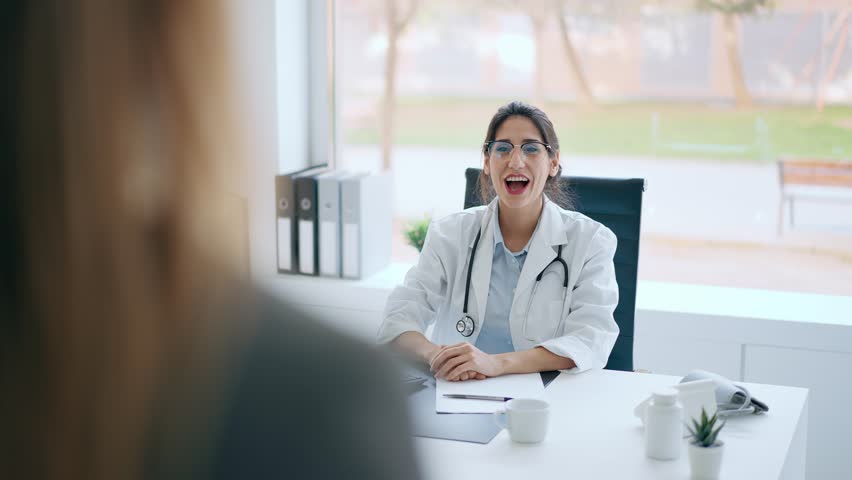 Video of beautiful cheerful female doctor talking while explaining medical treatment to patient in the consultation.