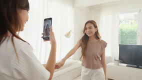 Two Happy Asian generation z woman friends vlogger influencer content creator enjoy and fun using smartphone live streaming viral video cover dance on social media application in living room at home.