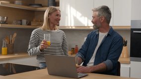 Caucasian happy family love couple middle-aged adult wife husband woman man drinking fresh healthy vitamin orange juice shopping with laptop at kitchen home talking laughing order food delivery online - Powered by Shutterstock - Get 15% off with code: PIKWIZARD15