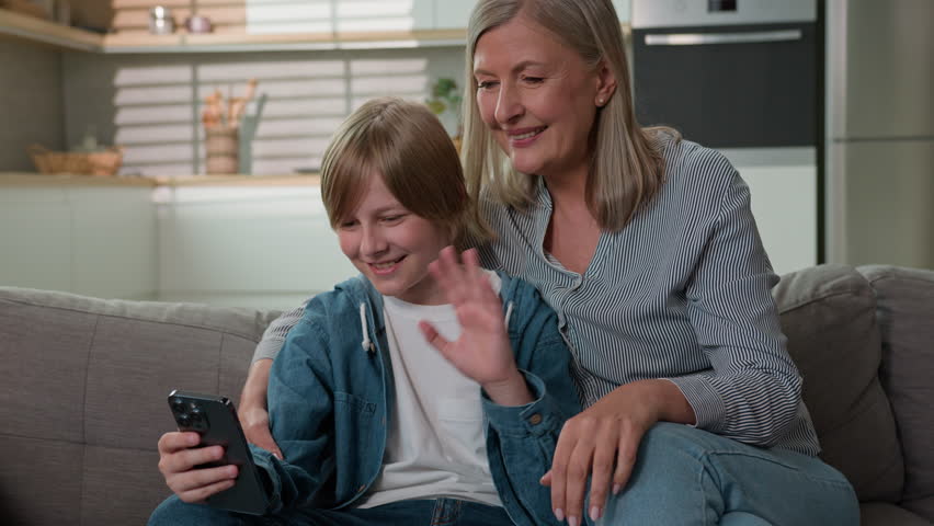 Senior caucasian woman grandmother with grandson talking via video call using mobile phone on couch at home smiling grandmother and grandchild boy communicate online conference in family chat relation
