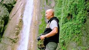 male photographer photographing waterfall giessbach in alpine mountains, fast flowing powerful stream of clear water, splashes scatter, concept of wild nature, natural resources, tourism