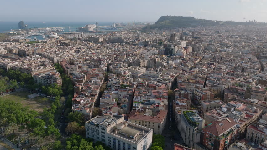 Aerial panoramic shot of large city at golden hour. Town development in urban borough and harbour in background. Barcelona, Spain