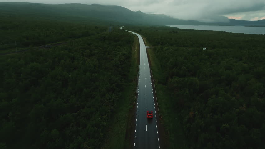 Epic top view of red SUV car driving alone on empty road amidst the beautiful Nordic landscape