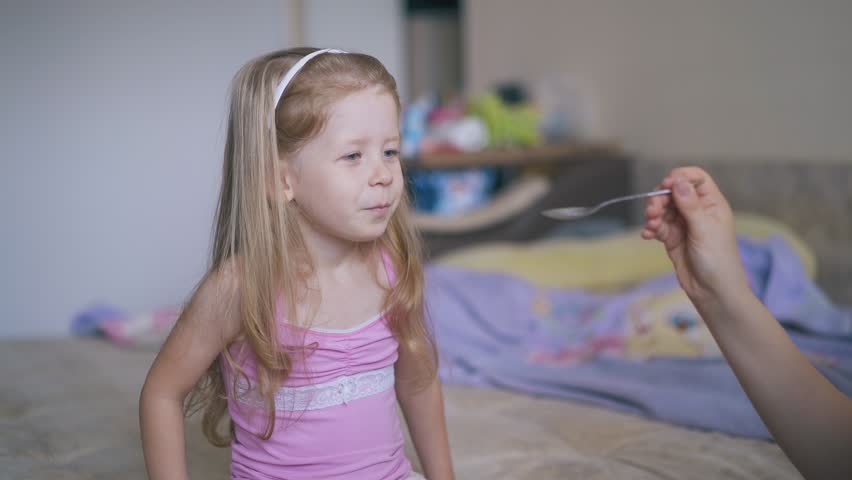 careful mother gives cough syrup to cute little girl in pink shirt on bed in spacious light room at home Royalty-Free Stock Footage #1105473717
