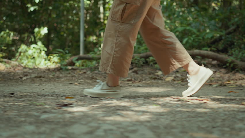 Low view - Close up of women feet in sneakers steps along path near forest, Legs of woman goes among trail at springtime, Female walks at wild at sunny day, Slow motion. Royalty-Free Stock Footage #1105474583