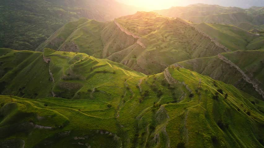 View of the green agricultural terraces and mountains at sunset.  Aerial drone view. Green fields near the Chokh village in Dagestan, Russia. Beautiful summer landscape.
