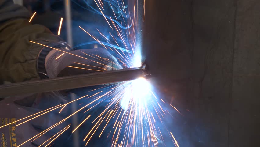 Engineer in a protective mask makes welding of metal parts for a future smelter, smoke and sparks around | Shutterstock HD Video #1105484383