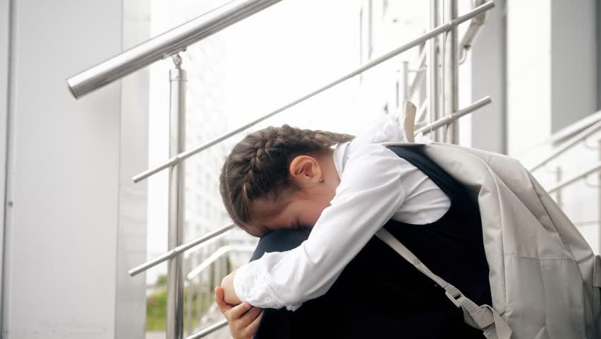 Brown-haired schoolgirl sitting on empty stairs cries remembering bullying moments. Girl with long braids afraid to attend school and see bullies Royalty-Free Stock Footage #1105486641