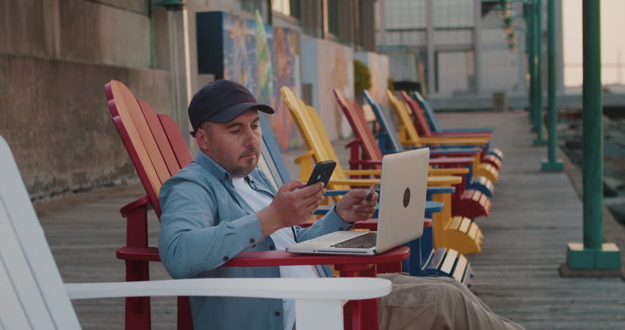 Man in Bench Looks at Goods in an Online Store, Buys Goods and Pays with a Credit Card. Man in Nature Lies in aBench on the Ocean Using a Laptop Buys in an Online Store.