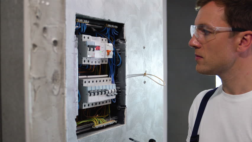 Professional electrician sets up electricity in the apartment. Electrician repairing electrical box and using screwdriver in corridor