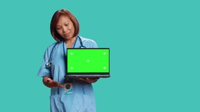 Cheerful nurse showing medical instructions video on laptop mock up chroma key green screen. Hospital employee presenting explanatory healthcare tape on gadget, isolated over blue studio background