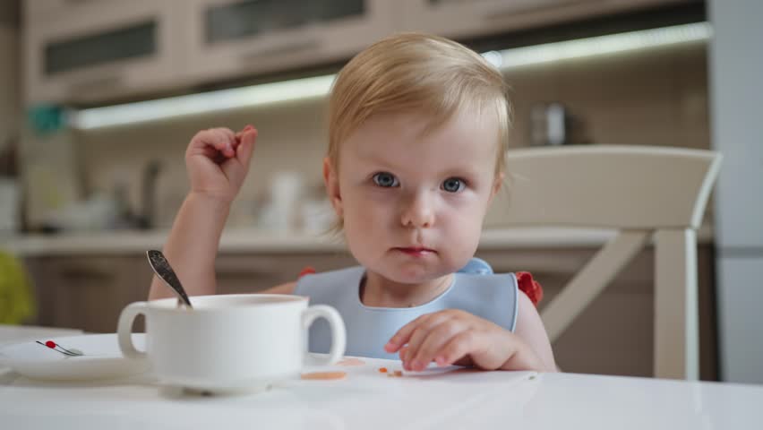 Funny little baby girl child having fun and smiling while having breakfast in the kitchen. Portrait of a playful and energetic happy little child. Royalty-Free Stock Footage #1105490385