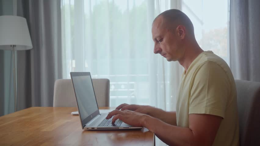 Serious man is using laptop texting enjoying friendly communication at home at table. Modern technology, internet and people concept. Thoughtful serious man at home office desk with laptop thinking Royalty-Free Stock Footage #1105491597