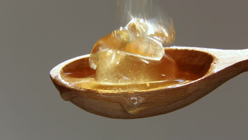 Thick, fresh honey pours on a wooden spoon in bright sunlight. Natural, sweet food. A thick stream of honey shimmers in a spoon illuminated by the sun. Macro. Close-up. Royalty-Free Stock Footage #1105500529
