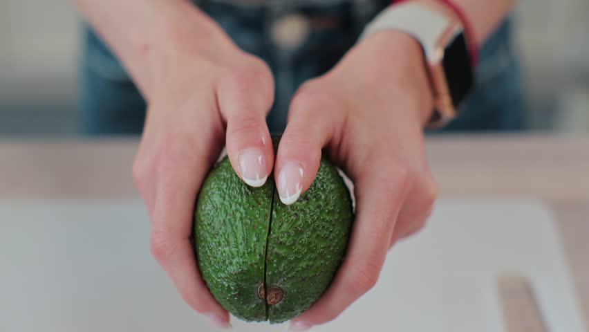 Close-up of a woman holding half of fresh ripe avocado in hand, top view.