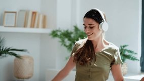 Video of happy woman listening to music with headphone while dancing in the living room at home.