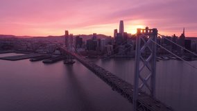 Scenic establishing shot of downtown San Francisco at dusk with beautiful pink clouds in sky at golden sunset. Traffic at Bay Bridge in direction of city. Epic cityscape view with skyscraper buildings