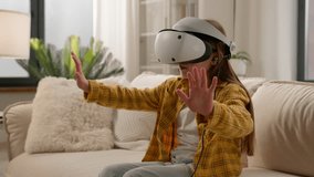 Funny caucasian kid girl child schoolgirl having fun in virtual reality headset at home couch playing online video game in world metaverse using innovative technology VR glasses exploring cyberspace
