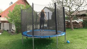 Girl is jumping on a trampoline in her backyard with green grass in the country house