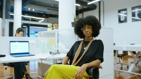 Young African-American businesswoman with black curly hair sitting at office cubicle and posing at camera during working day. Zoom shot, video portrait
