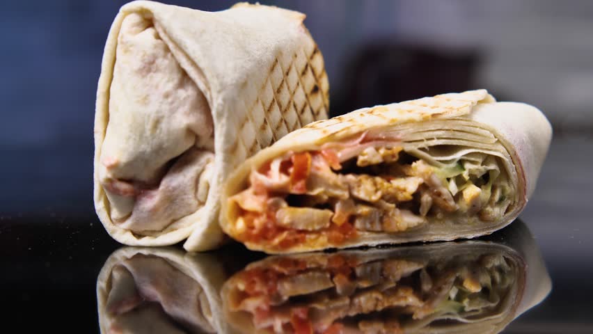 Shawarma split in two on a black mirrored surface. Camera rotates around. Parallax effect. Sharp zoom in and out. Beef gyros. A delicious Arabic doner kebab. Traditional Turkish food. Greek gyros Royalty-Free Stock Footage #1105523235