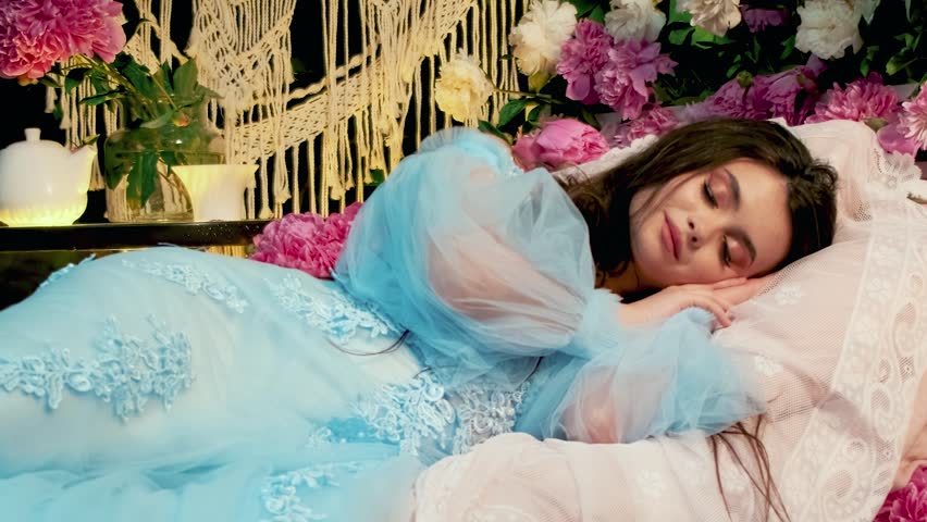 Art portrait happy fairy tale princess sleeping beauty face fashion model lies on bed. Young Fantasy woman resting eyes closed. Blue old style dress. natural Pink white peony flowers summer nature.