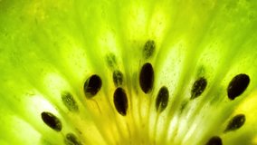 Macro video showcasing a half kiwi fruit's green flesh with an intricate pattern of tiny black seeds, glistening under soft lighting, revealing its juicy and refreshing texture. Kiwi background
