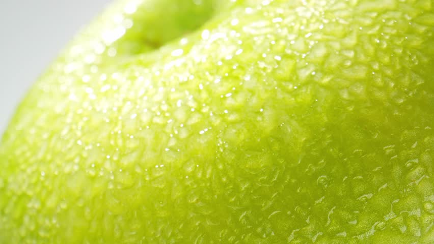 Capturing the individual droplets in exquisite detail. The smooth curves of the apple's skin are magnified, revealing tiny imperfections that only enhance its organic charm. Green apple background. 4K
