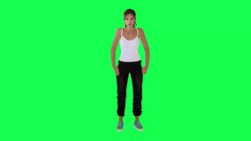 English woman in white dress black pants with blue shoes picks something up from the floor and looks at it from opposite angle on green screen