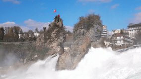 Water falls and drops scatter in different directions on Rhine Falls against old town in Switzerland