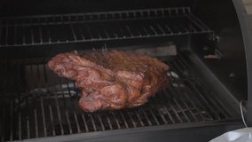 This video shows large smoked pork meat being taken out of a smoker with tongs.