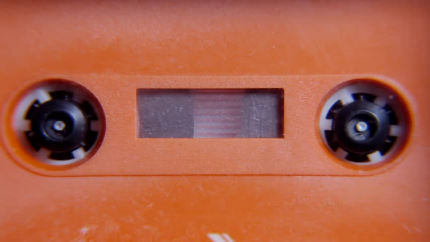 Rewinding an old orange plastic cassette tape inside a deck. Obsolete vintage audio technology. Front detail shot.
 Royalty-Free Stock Footage #1105546569