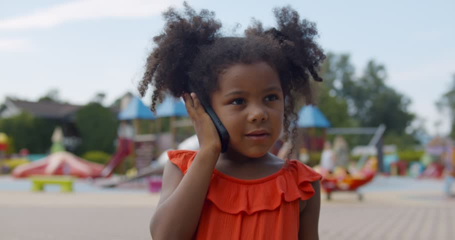 Pretty little African-American-American girl talking on mobile phone smiling happily outdoors in summer. Portrait of cute preschool girl having phone call at playground | Shutterstock HD Video #1105549037