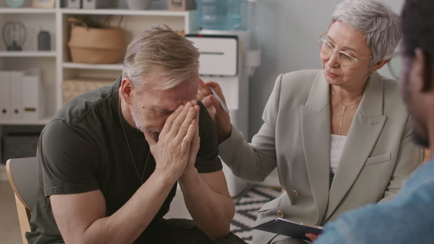 Medium shot of mature Caucasian soldier with PTSD crying during group therapy session with supportive psychologist | Shutterstock HD Video #1105549737